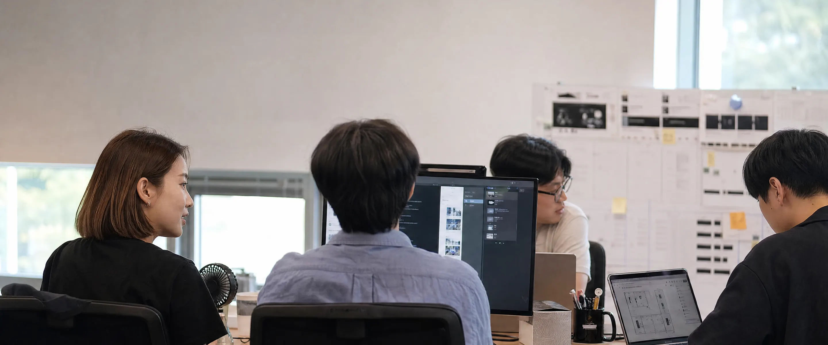 창가 자연광이 드는 사무실에서 각자 자리에 앉아 일하는 사람들의 뒷모습